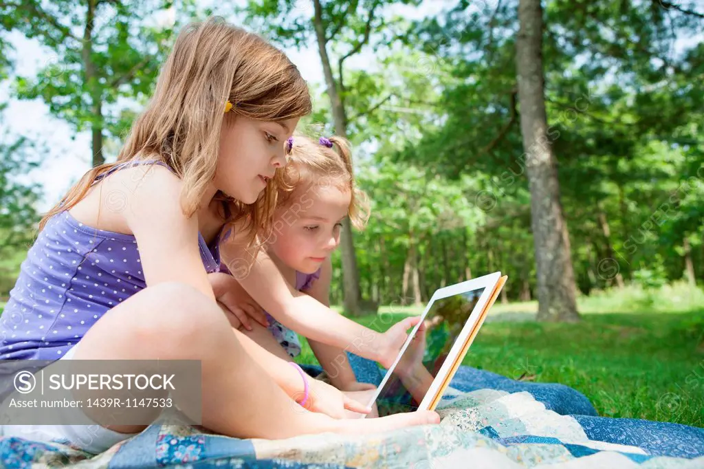 Two girls sitting on picnic blanket with digital tablet