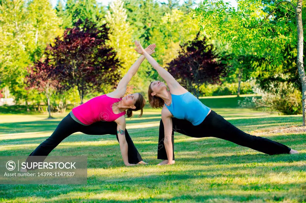 Two women practising yoga together in a park