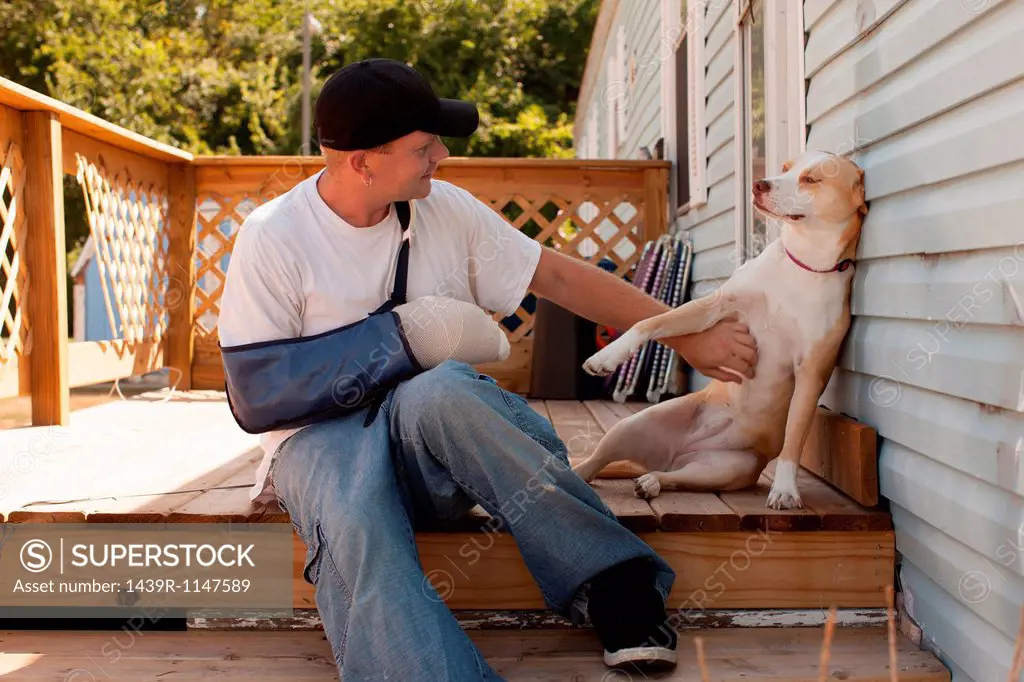 Man outside house with arm in sling and dog