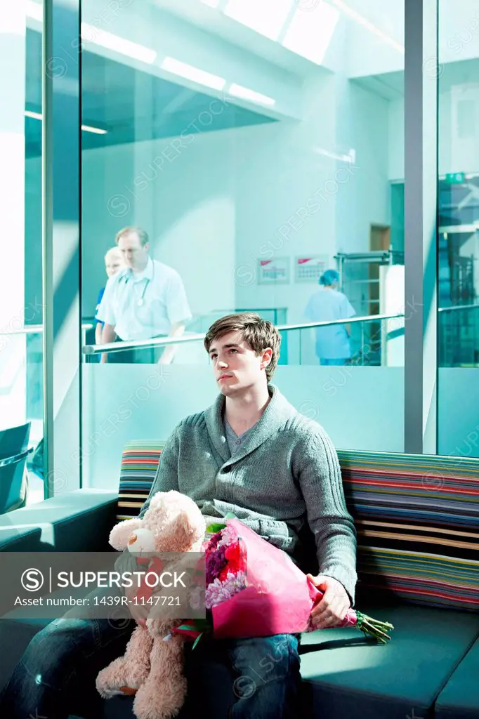 Man in hospital waiting room with bouquet and teddy bear