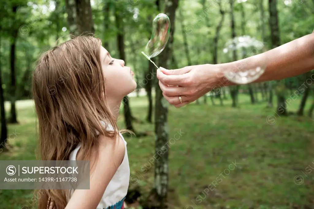 Woman holding bubble wand, girl blowing bubble