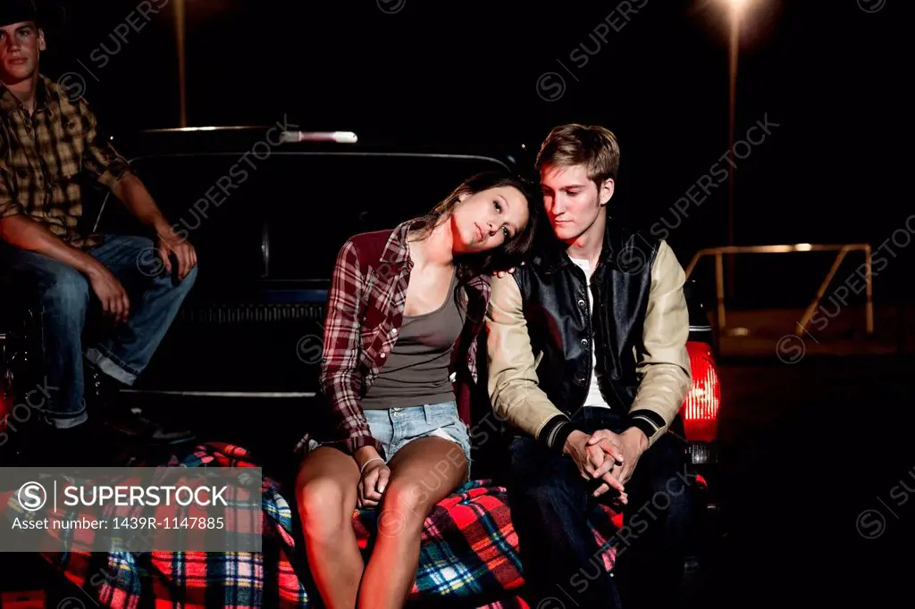 Couple sitting on tailgate of car at night