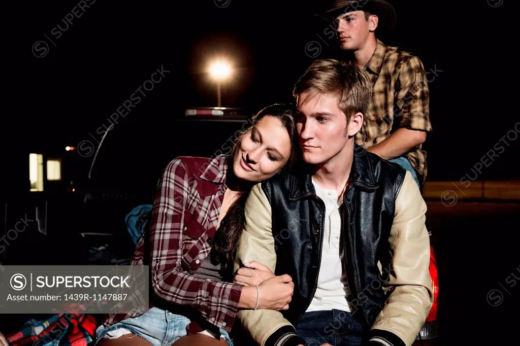 Couple sitting on tailgate of car at night