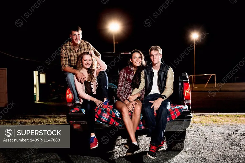 Portrait of friends sitting on tailgate of car at night
