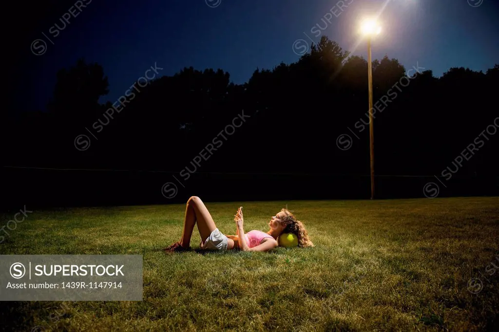 Girl using cell phone lying on soccer pitch at night