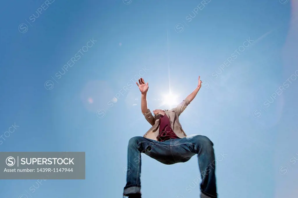 Young man jumping against blue sky, low angle