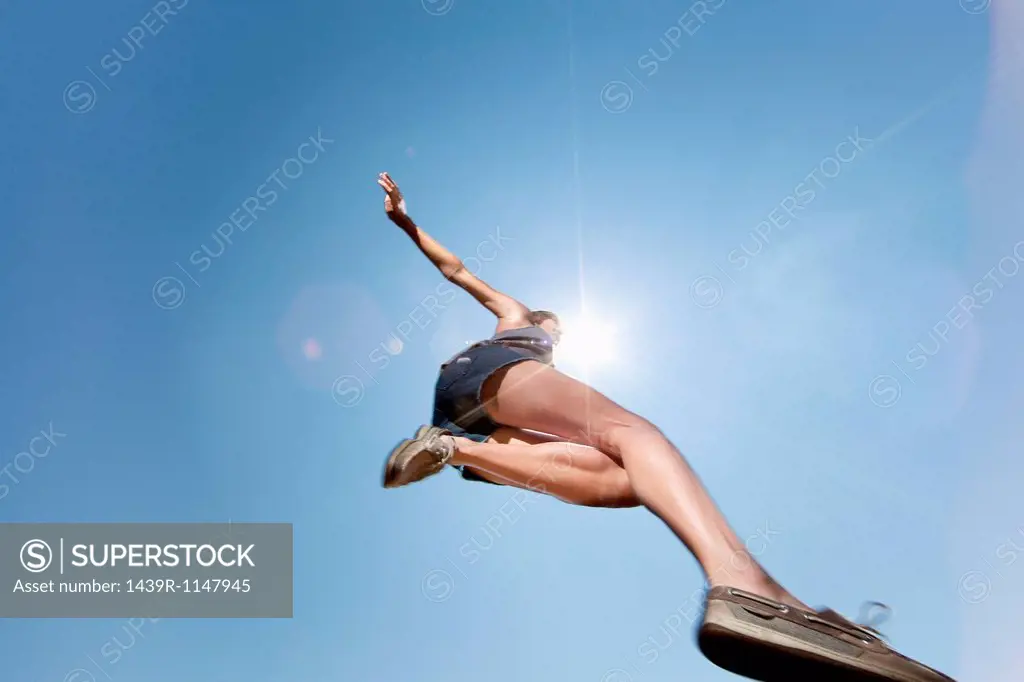 Girl jumping against blue sky, low angle