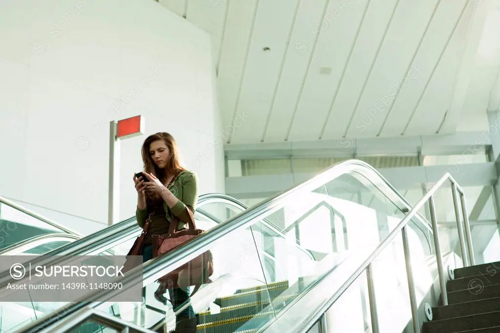 Young woman on escalator using smartphone