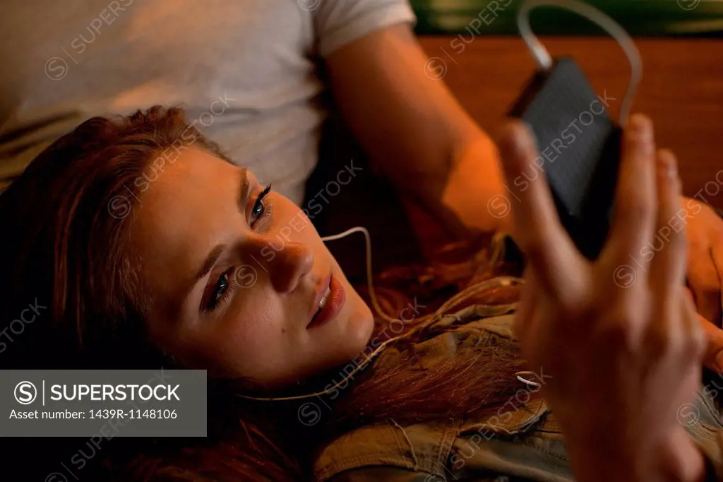 Young woman listening to music, lying on boyfriend´s lap