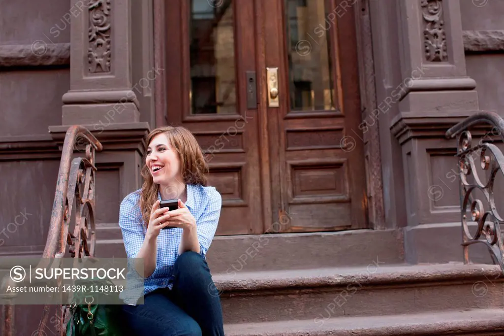 Young woman in steps of building with cellphone