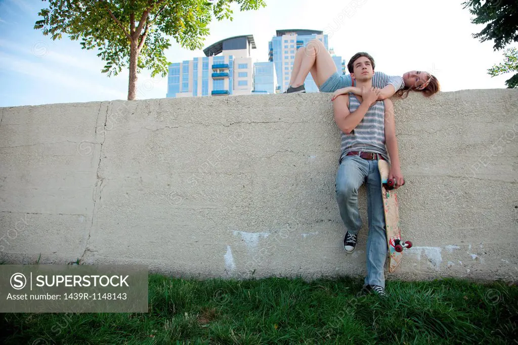 Young woman lying on wall with skateboarder