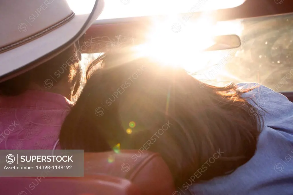 Woman resting head on boyfriend´s shoulder as he drives in sunlight
