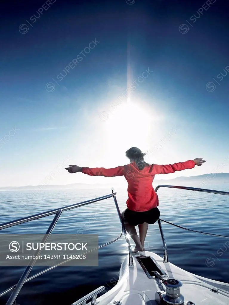 Woman on bow of sailing boat with arms outstretched