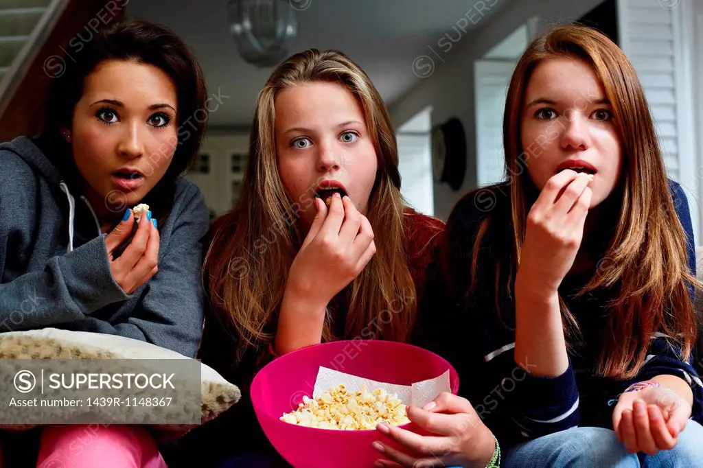 Teenage girls watching horror movie with popcorn