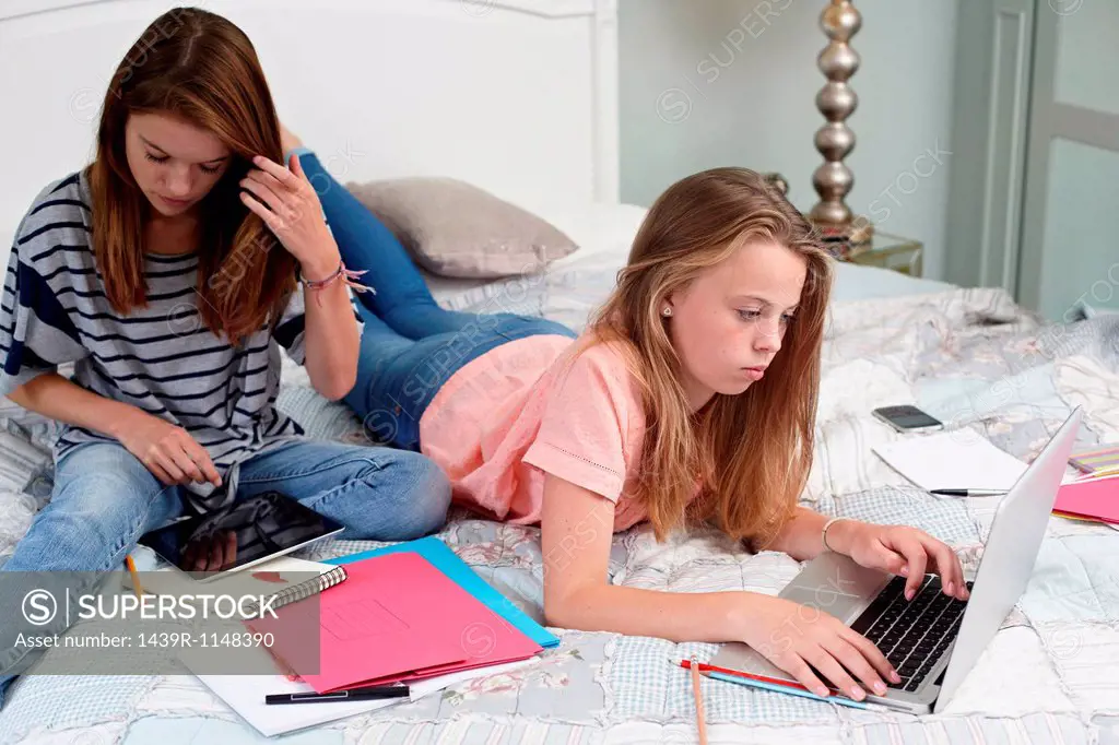 Teenage girls using laptop and digital tablet on bed