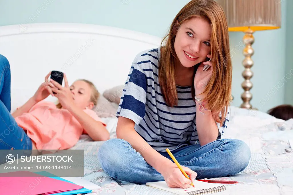 Teenage girl sitting on bed, using cellphone