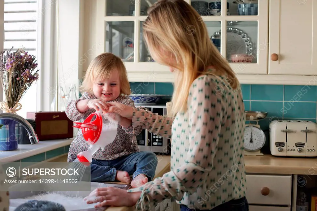Mother washing up, daughter pouring water