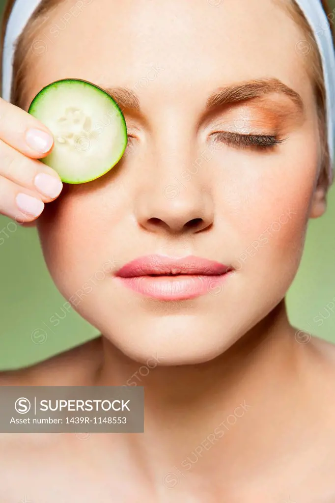 Woman covering eye with piece of cucumber