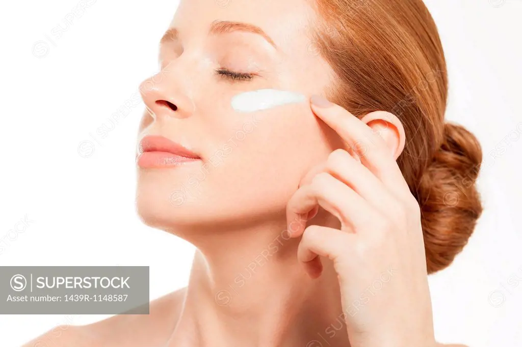 Woman applying moisturiser with eyes closed