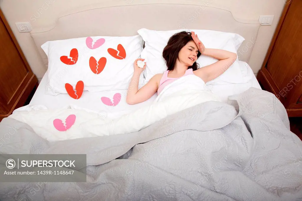 Woman crying in bed with broken heart shapes on bedclothes