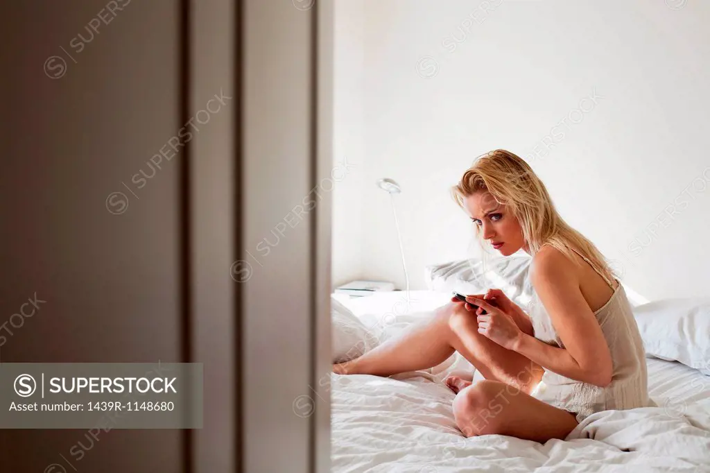 Young woman sitting on bed with cellphone