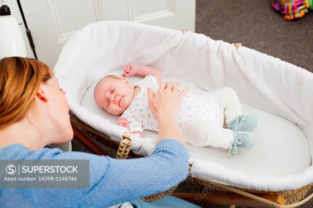 Mother comforting newborn daughter in bassinet
