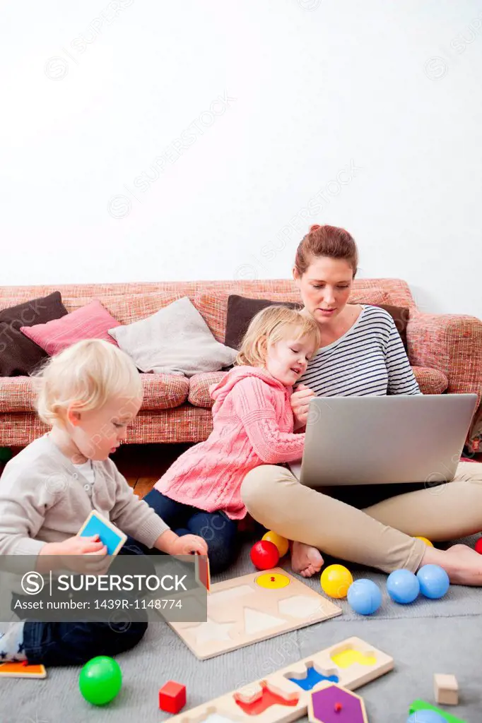 Mother using laptop, children playing