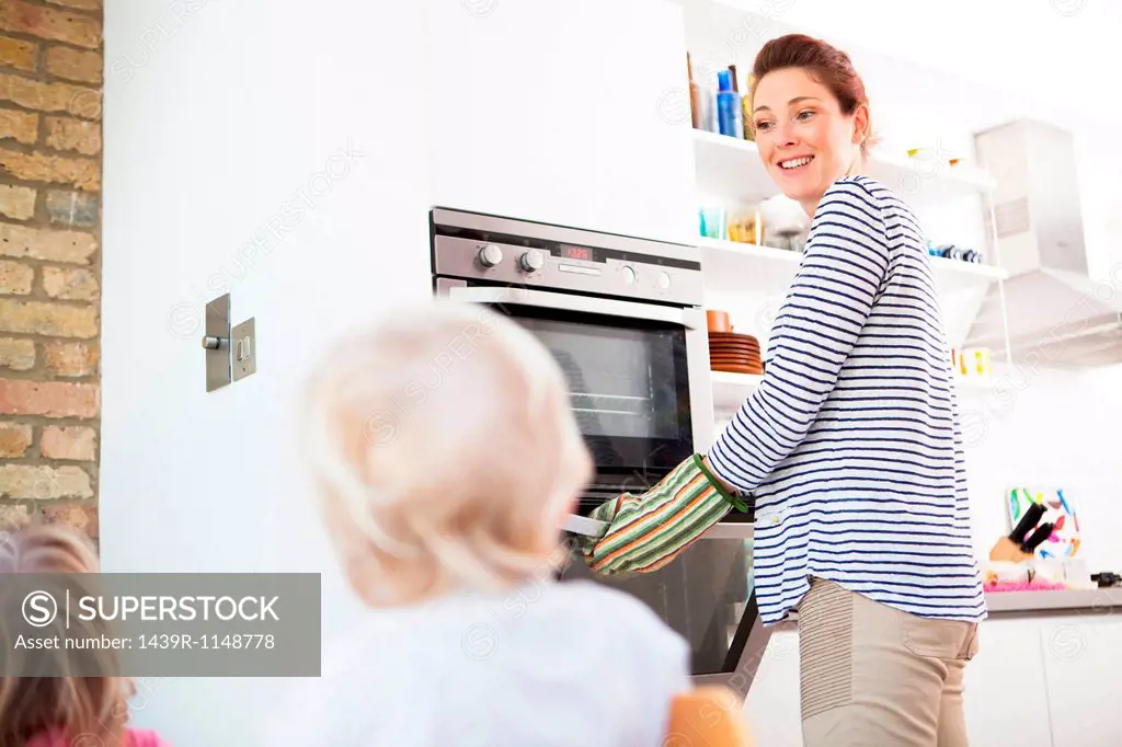 Mother wearing oven gloves opening oven
