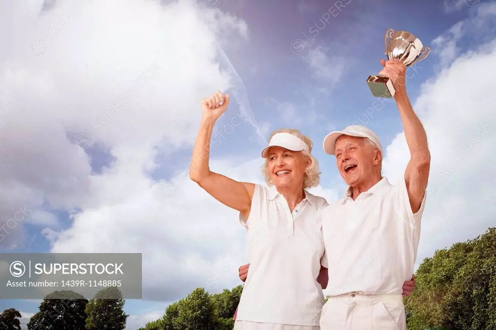 Senior couple holding tennis trophy and cheering
