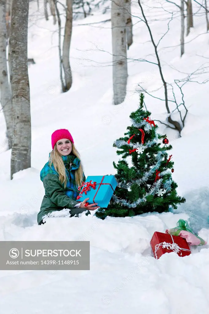 Woman sitting by christmas tree with gift