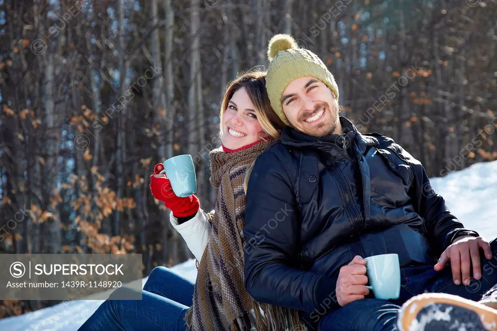 Portrait of couple sitting in snow with hot drinks