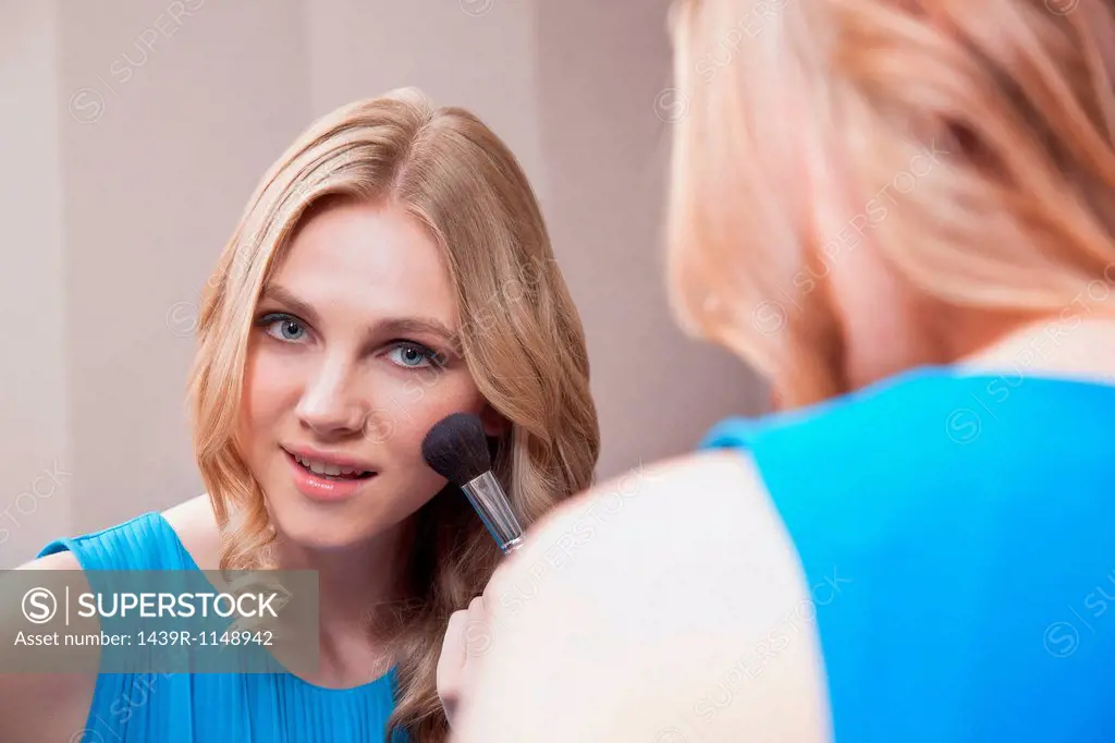Young woman applying blusher in the mirror