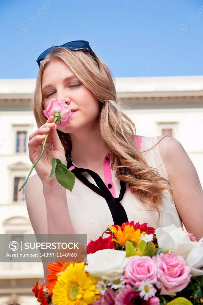 Young woman smelling rose from bouquet of flowers, eyes closed