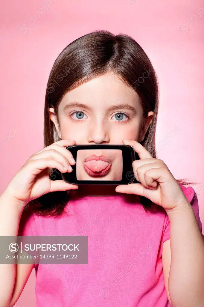 Girl holding smartphone over mouth, sticking out tongue