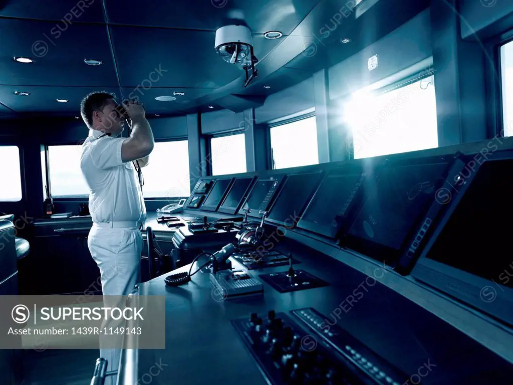 Captain in cockpit of motor yacht, using binoculars