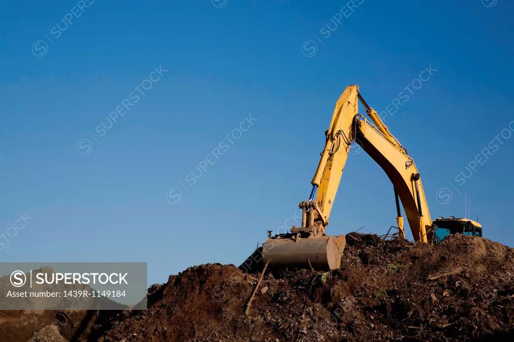 Excavator working on pile of topsoil
