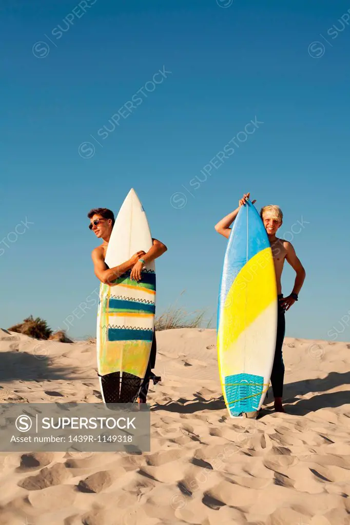 Two young men standing behind surfboards on beach