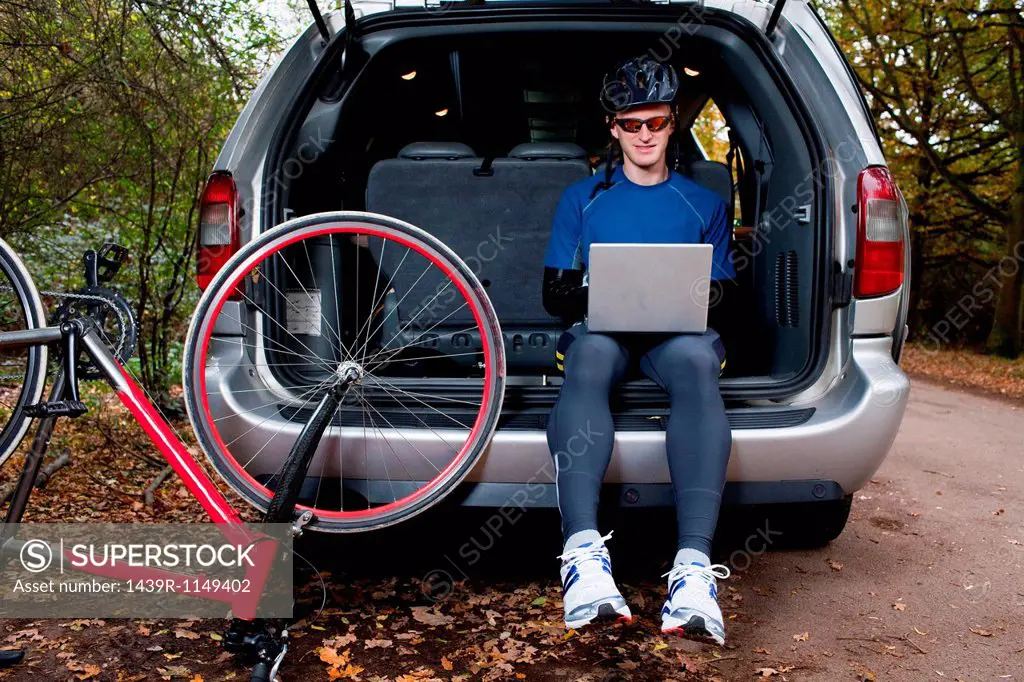 Cyclist using laptop from boot of car