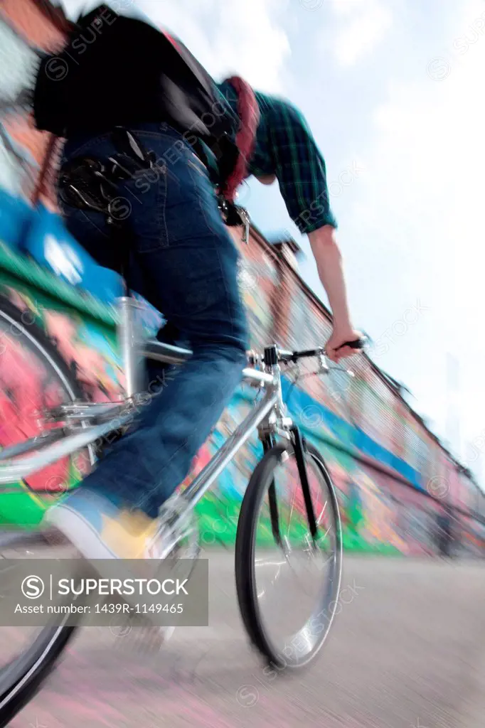 Mid adult cyclist riding bike across bridge