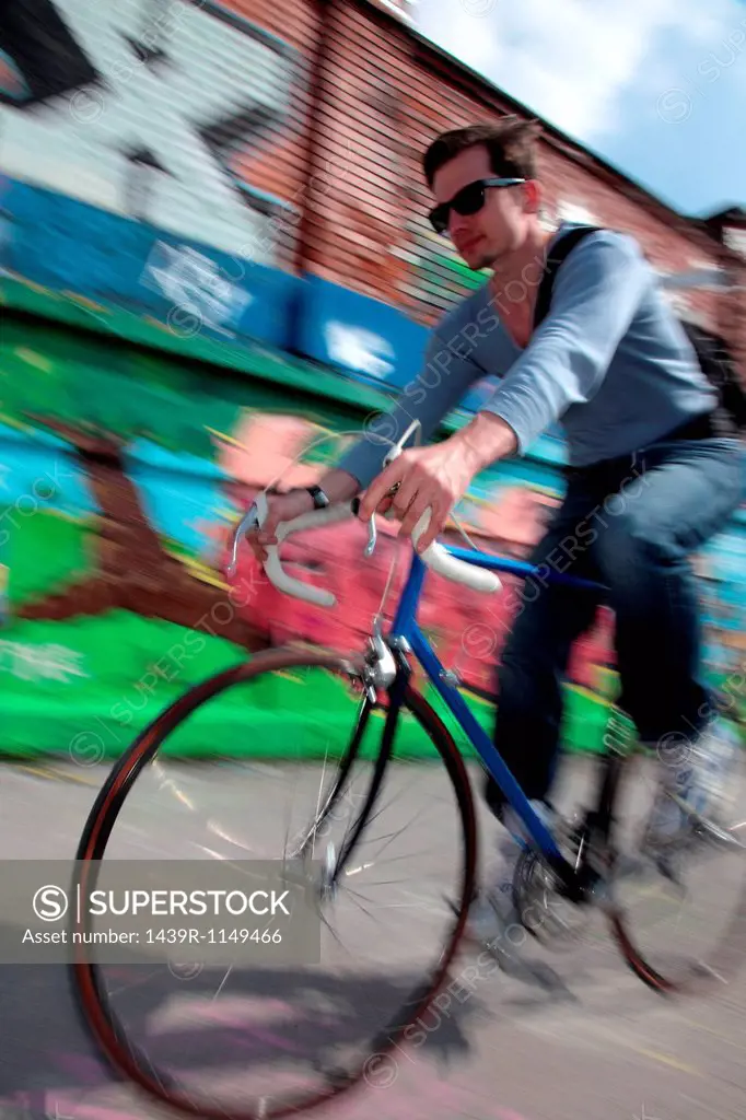 Mid adult cyclist riding passed graffiti