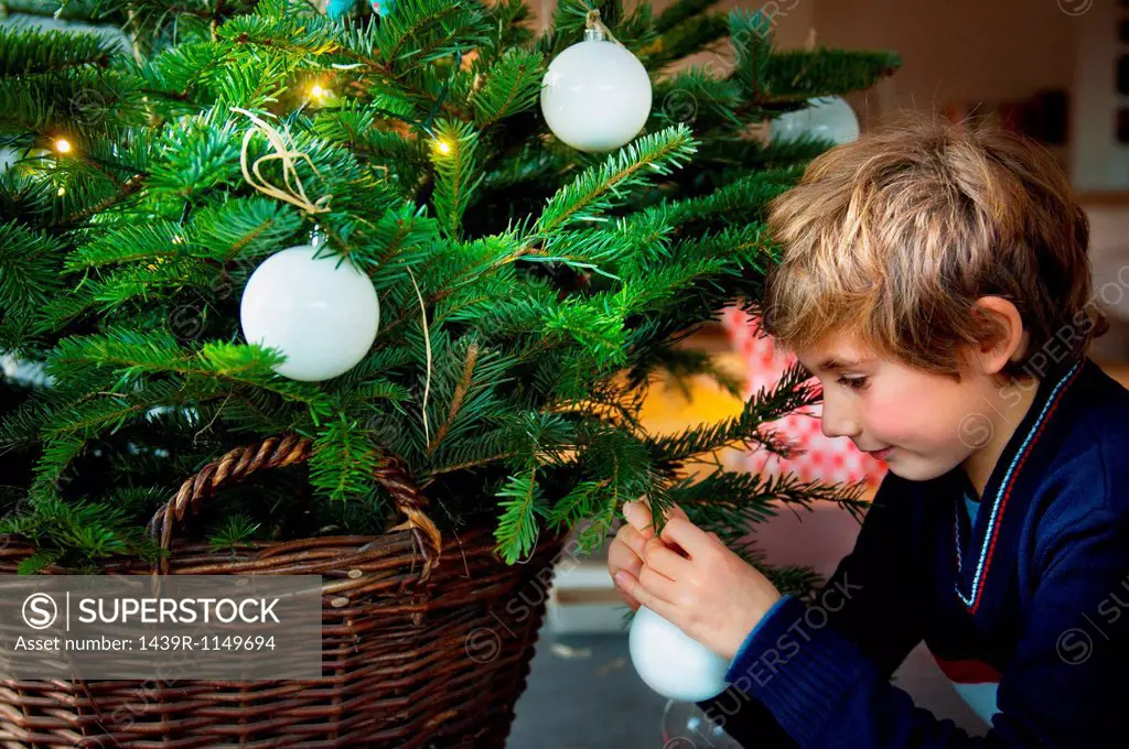 Boy decorating Christmas tree with baubles at home