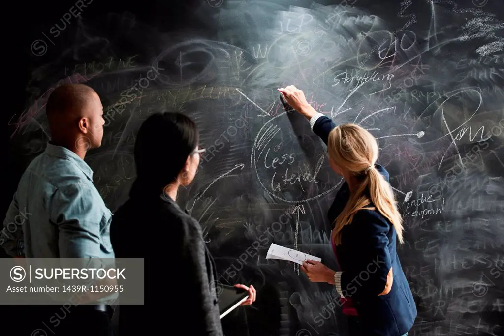 Woman writing on blackboard, colleagues watching
