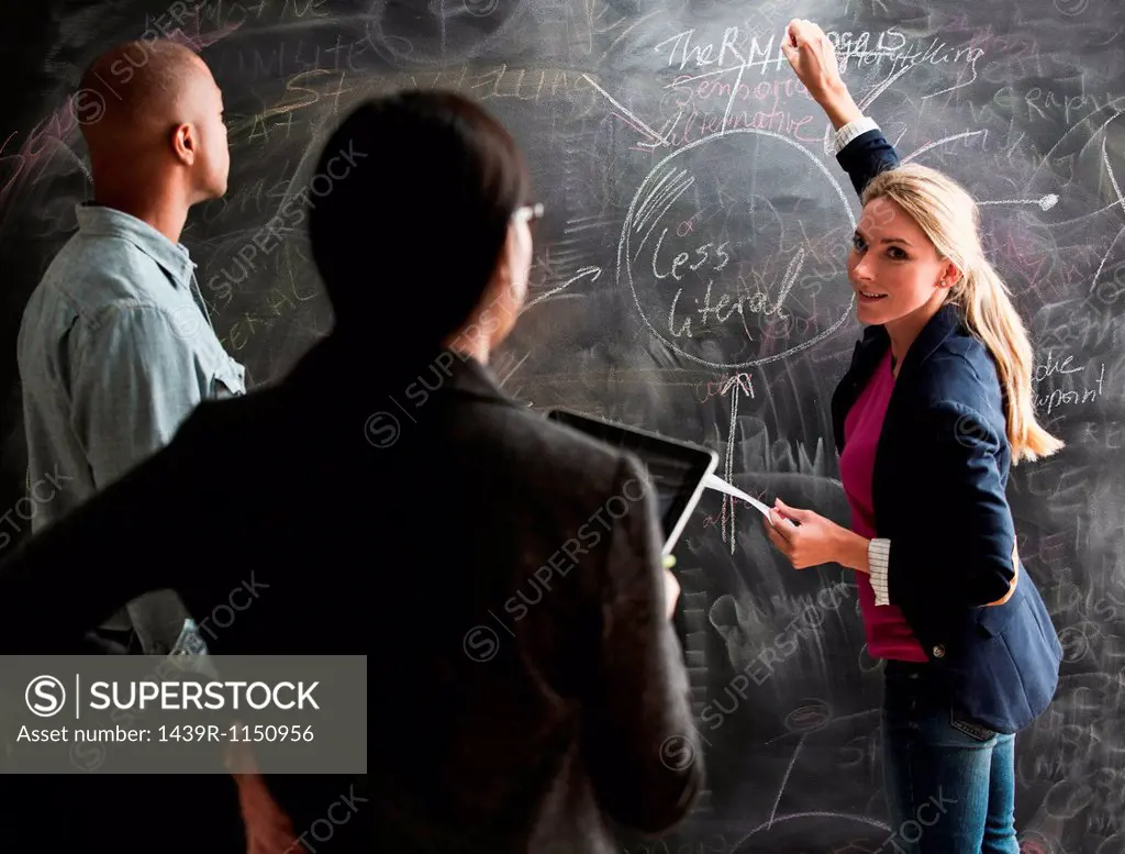 Woman writing on blackboard, colleagues watching