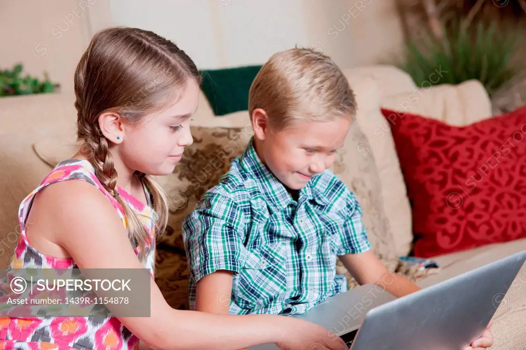 Children using laptop together on sofa
