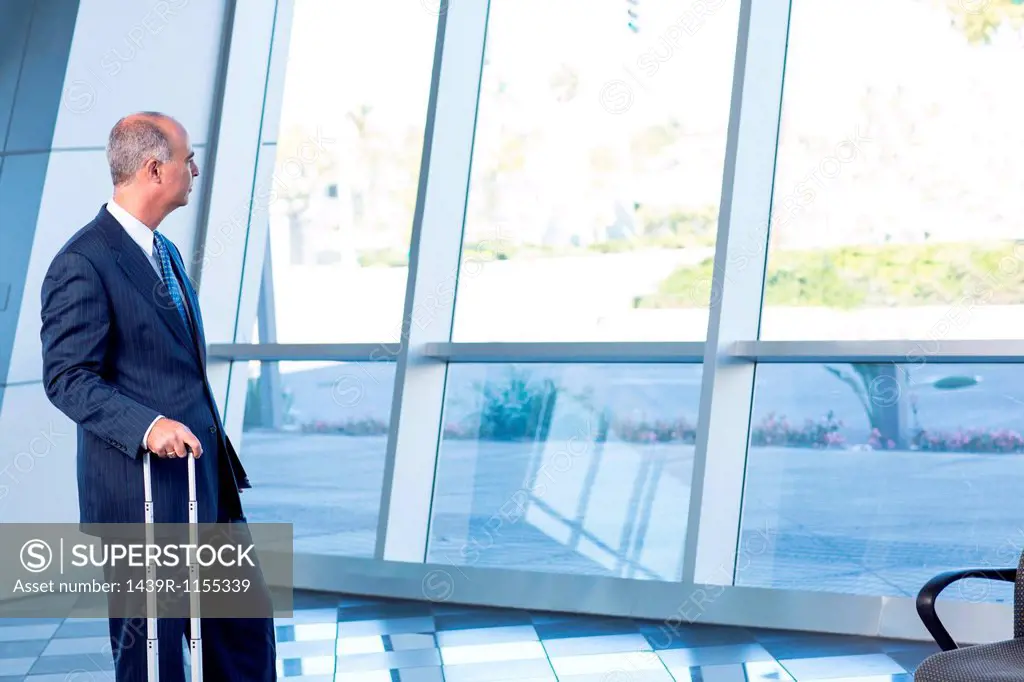 Mature businessman with suitcase looking through window
