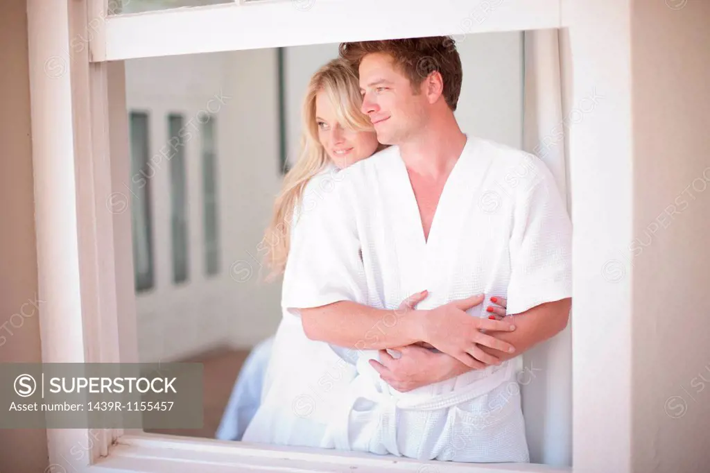 Young couple wearing bathrobes by window