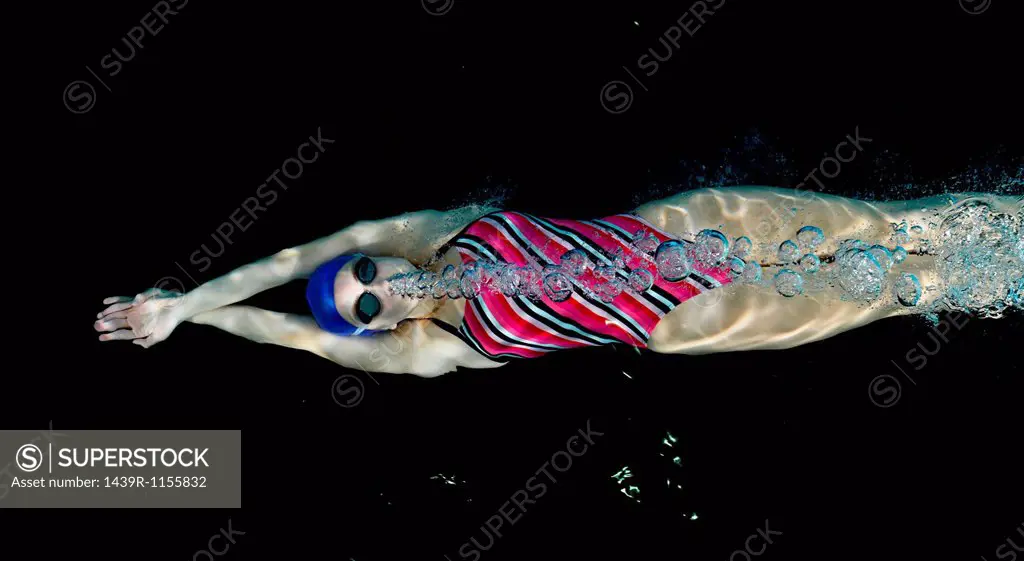 Teenage girl swimming underwater blowing bubbles