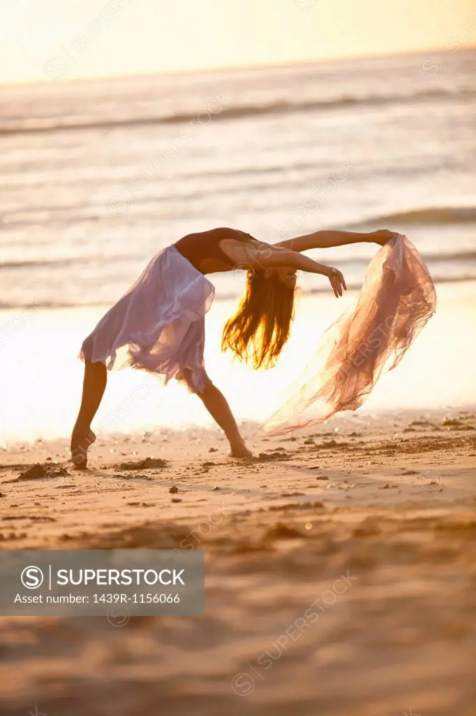 Young woman dancing on sunlit beach