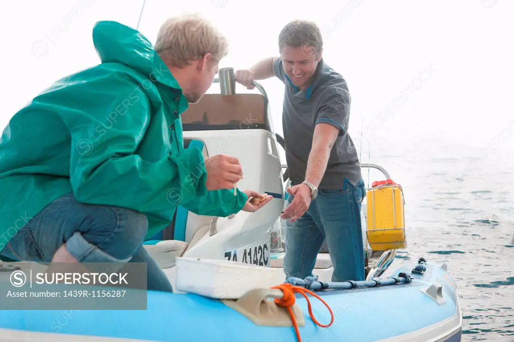 Two young men looking at fishing bait in dinghy