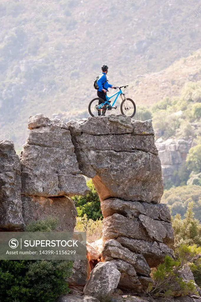 Young man standing on rock formation with mountain bike